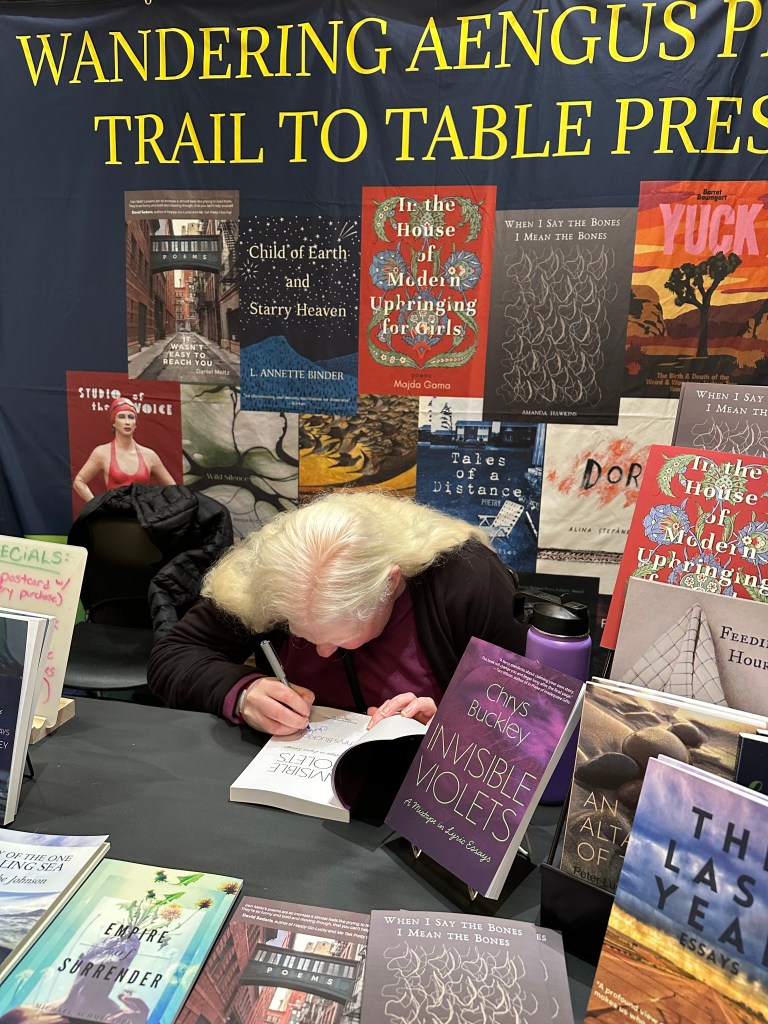 Chrys Buckley signing advanced reader copies of her book Invisible Violets at the Wandering Aengus Press booth at the Portland Book Fest
